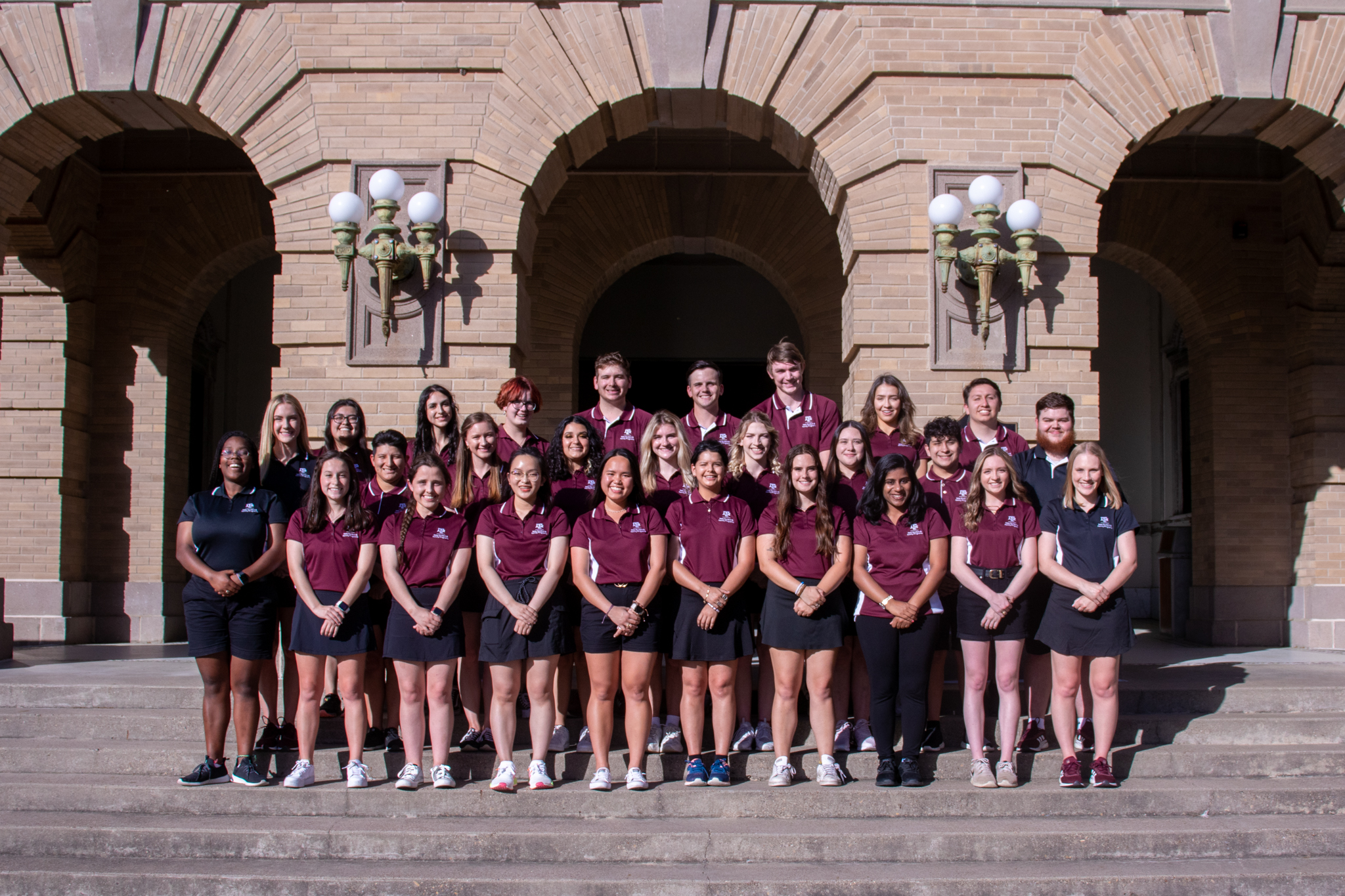 Group photo of the Aggie Orientation Leaders in their uniforms standing on the steps of the Academic Building on a sunny day.