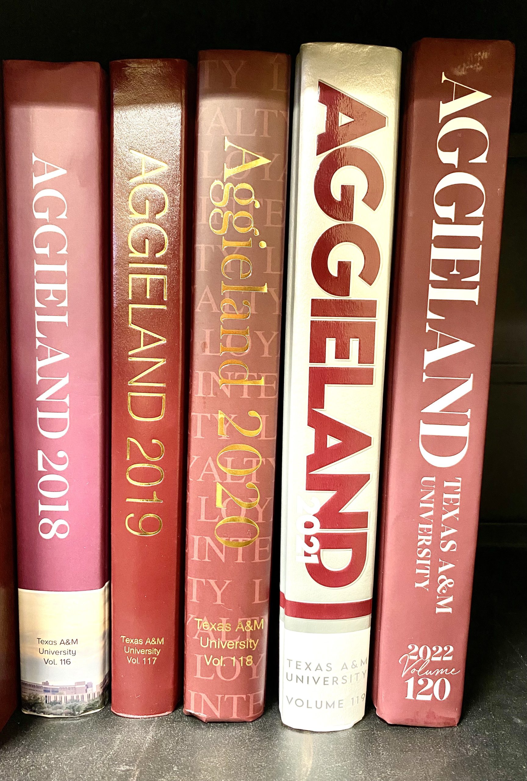 Various versions of the Aggieland Yearbook sitting on a bookshelf.