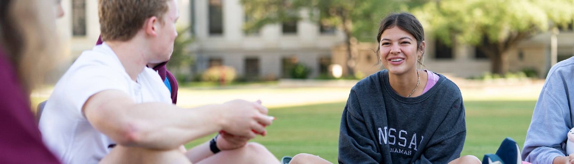 Students sitting in a circle on the grass in Academic Plaza smiling and having a conversation.