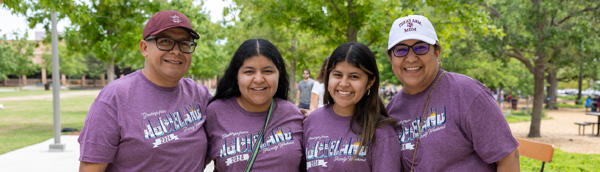 A family of four Aggies at Aggie Park, smiling and wearing matching Family Weekend t-shirts.