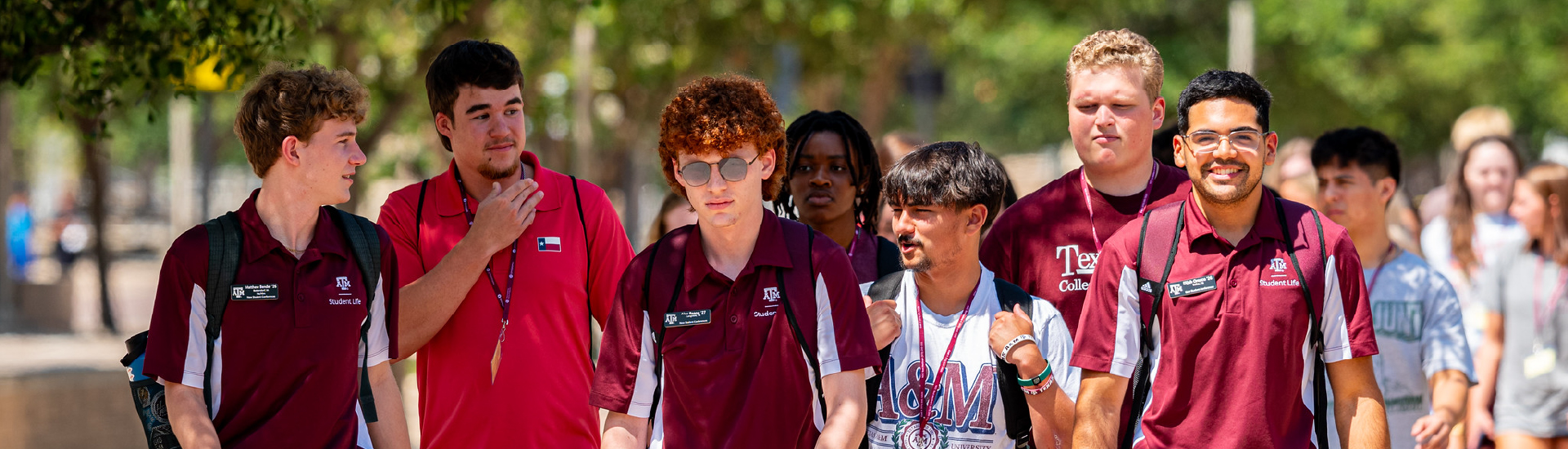 Aggie Orientation Leaders in uniform leading a group of new students across campus on a sunny day.