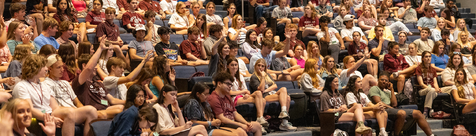 Many students sitting in Rudder Theatre on-campus listening to a presentation. Several in the audience are raising their hands in answer to a question.