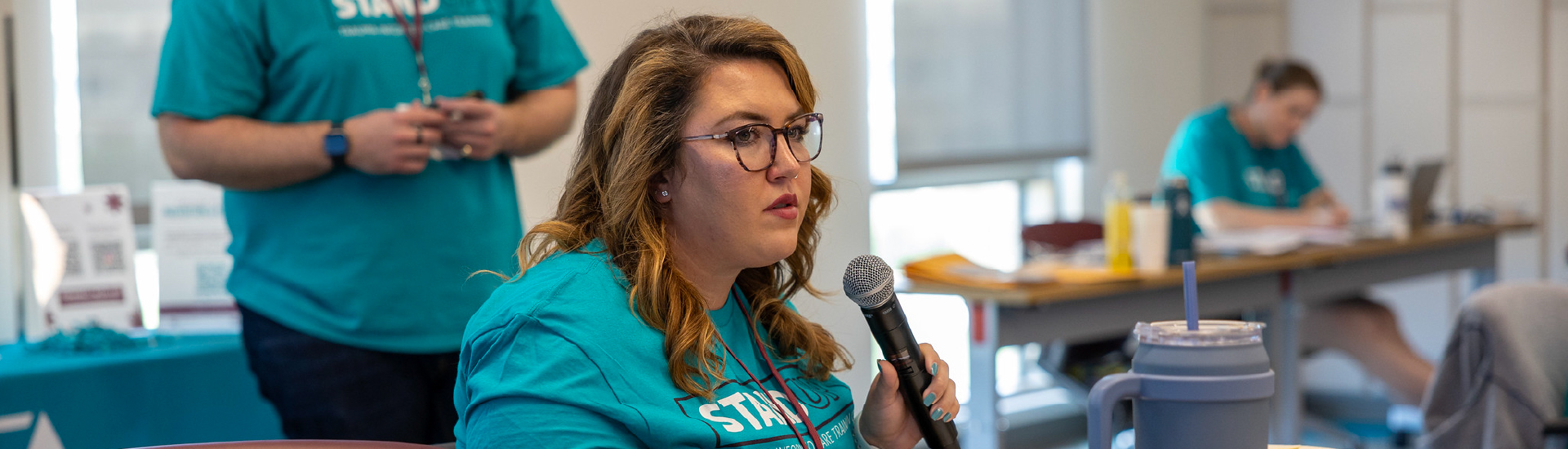 A staff member speaking into a microphone at a Stand Up workshop.