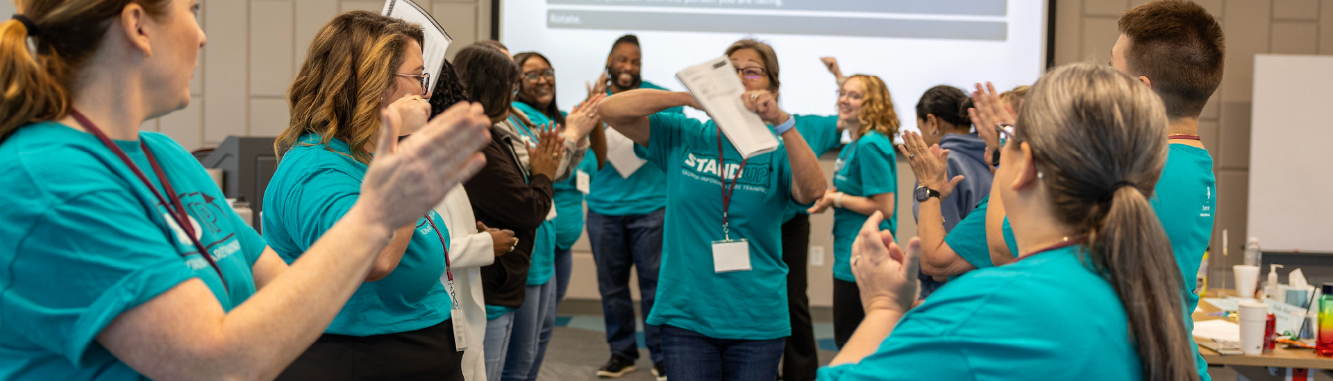 Several staff members in a circle cheering on another staff member during a Stand Up workshop. Some are dancing around and some are clapping.