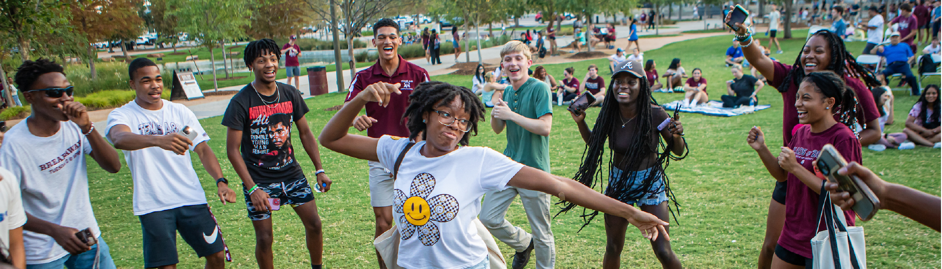 Students standing in a circle outside with one dancing in the middle.