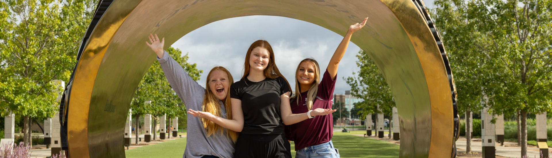 Three girls posing in front of the large Aggie Ring replica.