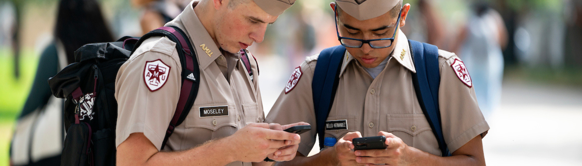 Two Texas A&M Cadets looking down at their phones standing in Aggie Park.