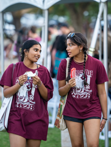 Two students walking and chatting to each other while eating ice cream.