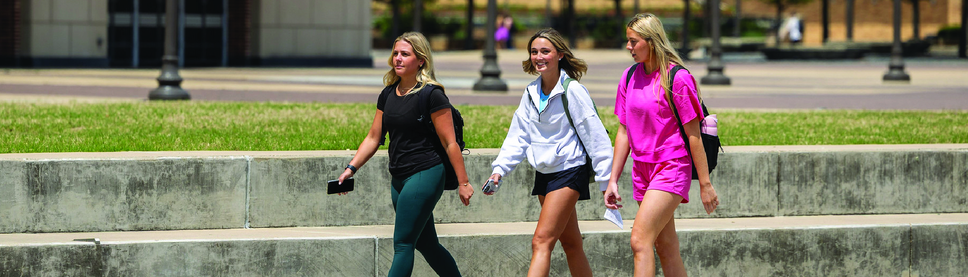 Three Aggie students walking by Kyle Field on campus, chatting as they go.