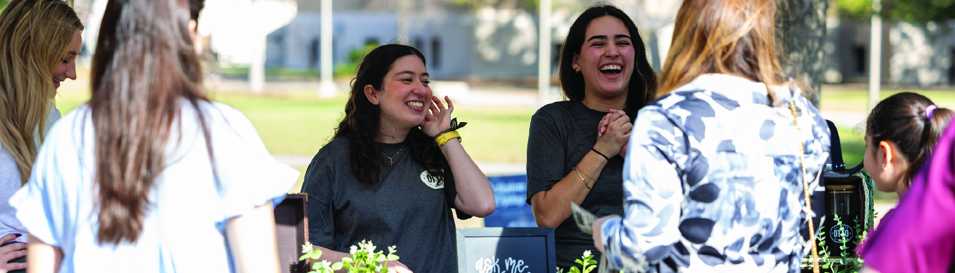 Aggie families engaging with a Good Neighbor Network property. Staff are behind a table laughing and smiling with the families on Aggieland Saturday.