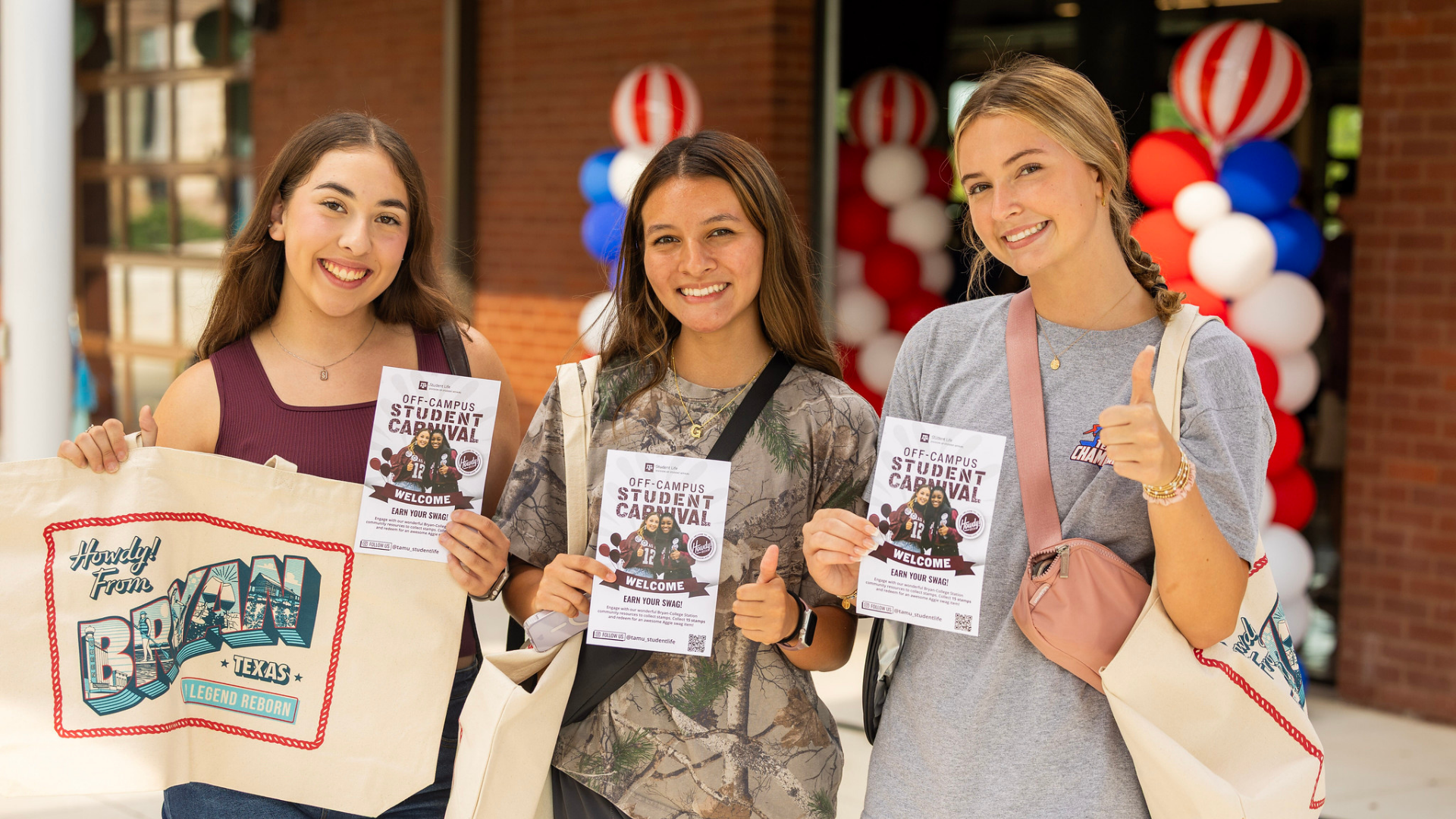 Three students holding Off-Campus Student Carnival flyers and Howdy from Bryan canvas tote bags indoors with red, white, and blue balloon decorations in background